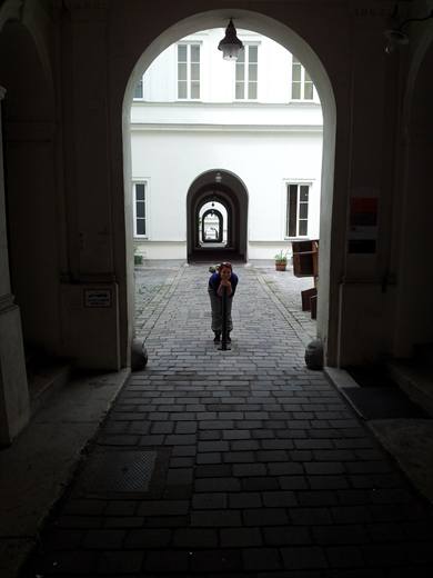 Julia lehnt sich im Arkadenhof aufs Pfostengeländer, Kinn auf die Hände gestützt