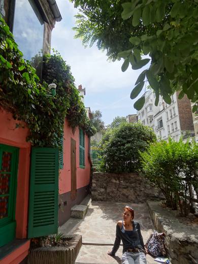 Sonnenpause in Montmartre, Julia sitzt vor dem rosa Häuschen mit den grünen Fensterläden