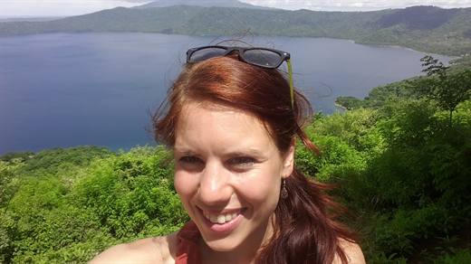 Julia mit Wind in den Haaren, hinter ihr leuchtet ein Kratersee in tiefem Blau