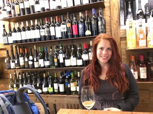 Ein Glas Weisswein vor einer ganzen Wand voller Flaschen, Julia hat die Qual der Wahl gemeistert